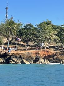 A scenic view of a coastline with people enjoying the beach, surrounded by lush greenery and clear blue waters — perfect for island adventures.