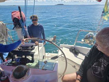 A group enjoys a sunny day on the water, with one person swimming nearby and others aboard the boat, creating a lively atmosphere perfect for adventure and relaxation.