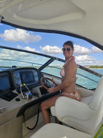 A woman enjoys steering the boat from the helm, showcasing the stylish interior and controls — perfect for navigating the open waters.