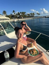Two friends enjoy a delicious meal on the deck of a boat under the sun, capturing the essence of a perfect day on the water.
