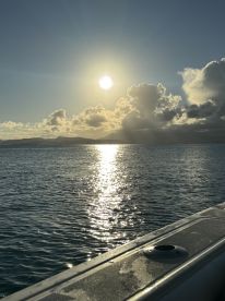 A serene sunset view over calm waters, showcasing the boat's edge while the sun reflects beautifully on the surface — perfect for tranquil evening cruises.