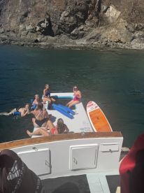 A lively group enjoys a fun day on the water, relaxing on floating mats and paddleboards, surrounded by beautiful rocky scenery.