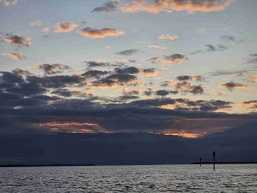 A stunning sunset over the water, showcasing vibrant colors and a serene coastline — perfect for capturing the beauty of nature during a boating trip.