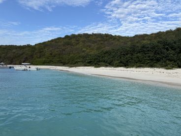 A picturesque view of a serene beach with boats anchored nearby, showcasing the beauty of the coastline and inviting waters — perfect for a day of relaxation and exploration.