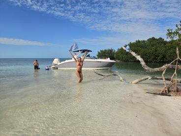A joyful moment captured at the beach with a woman celebrating in shallow water while a boat is anchored nearby, perfect for summer fun and water adventures.