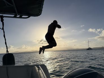 A person joyfully jumps into the water at sunset, capturing the essence of fun and adventure on a sailing trip.