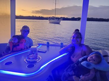 A joyful family celebrates a birthday on a boat at sunset, complete with a cake and life jackets for the little ones — a perfect setting for memorable moments on the water.