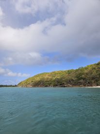 A serene view of a lush green coastline under a partly cloudy sky, showcasing the beauty of the island's natural landscape — perfect for eco tours and scenic boat trips.