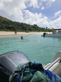 Guests enjoy a sunny day at the beach, with one person swimming in the clear waters while others walk along the shore — a perfect scene for a relaxing day on the water.