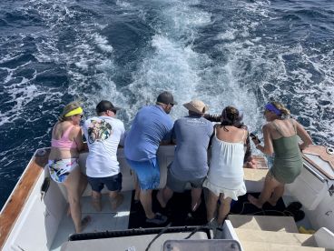 A lively group of friends leans over the side of a boat, enjoying a fishing adventure on the open ocean. The excitement of the day is palpable as they engage with the water.