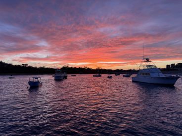 A stunning sunset view featuring multiple boats anchored in calm waters, creating a picturesque scene perfect for evening cruises.