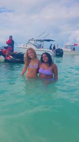 Two friends enjoy a refreshing swim in crystal-clear waters, surrounded by boats — a perfect day for beach fun and relaxation.