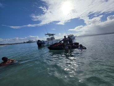 A lively group enjoys a sunny day on the water, posing on a jet ski while others swim nearby — perfect for a fun-filled aquatic adventure.