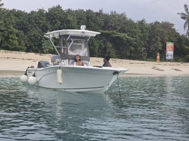 Two guests relax on a boat anchored near a serene beach, enjoying the tranquil waters and scenic surroundings — a perfect getaway for beach lovers.