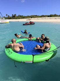 A lively group enjoys a floating mat in the clear waters, perfect for relaxation and fun under the sun at the beach.