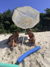 A cheerful group enjoys a sunny day at the beach, relaxing under an umbrella with snacks — perfect for a fun day out in the sun.