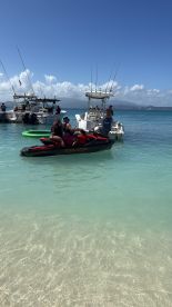 Two people enjoy a thrilling ride on a jet ski in clear waters, surrounded by boats — a perfect snapshot of summer fun on the water.