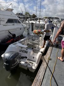 A group of individuals engages in activity at the dock with the boat 'La Ultima' in view, showcasing a vibrant day of fishing and fun on the water.