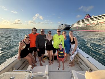 A joyful group poses together on a boat with a cruise ship in the background, capturing a memorable moment on the water.