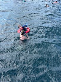 A joyful moment of a child floating on a raft while a parent enjoys the water, showcasing a fun family snorkeling experience.
