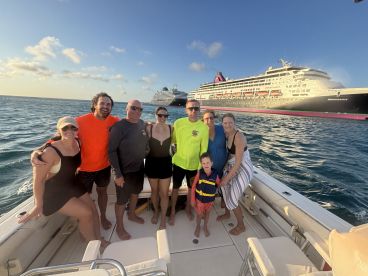 A joyful group poses on a boat with a cruise ship in the background, capturing a memorable moment of fun and togetherness on the water.