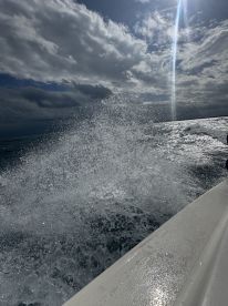 An unclear image capturing splashes of water, possibly from a moving boat, with cloudy skies in the background.