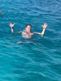 A man enjoys a refreshing swim in crystal-clear ocean waters, capturing the essence of a perfect day on the water.