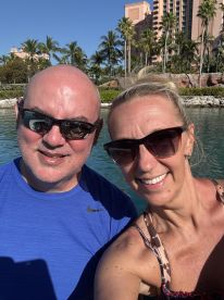 A cheerful couple takes a selfie on the water, capturing their joyful vacation moment against a backdrop of palm trees and luxury resorts.