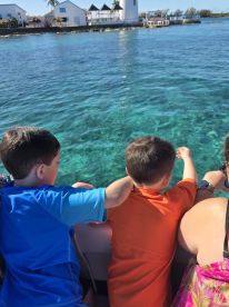 Two children lean over the side of a boat, excitedly pointing at the clear turquoise water — a perfect moment of family exploration on the water.