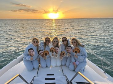 A group of friends celebrates at sunset on a yacht, holding playful masks — a perfect moment for fun and memories on the water.