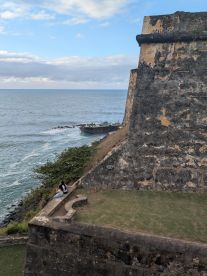 A couple enjoys the scenic view from a historic fort overlooking the ocean, capturing a moment of tranquility amidst stunning coastal scenery.