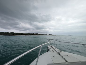 A serene view from the bow of a boat, showcasing the tranquil waters and distant shoreline under a cloudy sky — perfect for exploring coastal destinations.