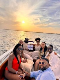 A joyful group enjoys a sunset boat party, capturing memorable moments against a stunning backdrop of the setting sun over the water.
