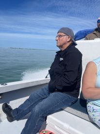 A man sits on a boat enjoying the ride, with a serene water backdrop and clear skies, capturing the essence of a relaxing day on the water.