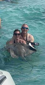 A couple joyfully interacts with a stingray in shallow waters, capturing a memorable wildlife experience during their aquatic adventure.
