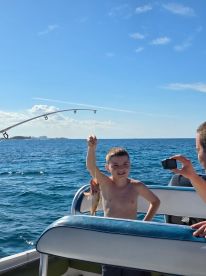 A young boy proudly holds up his catch while fishing on a boat, capturing a joyful moment of celebration on the water.