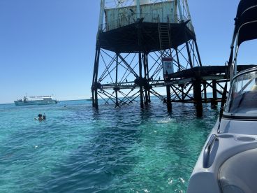 A vibrant scene featuring snorkelers enjoying the clear turquoise waters near a pier, with another boat in the background — perfect for water activities and group fun.