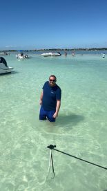 A man enjoys a sunny day in shallow waters surrounded by boats and other beachgoers, capturing the essence of a fun-filled day on the water.