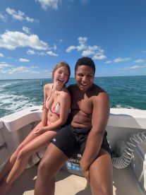 A joyful moment captured on a boat as a young couple shares laughter against a beautiful ocean backdrop, perfect for memorable summer adventures.