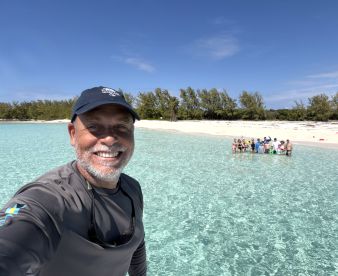 A smiling guide captures a moment with a group enjoying a sunny day at the beach, surrounded by crystal-clear waters — a perfect setting for memorable adventures.