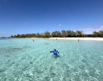 A vibrant scene at a beautiful beach with clear waters, featuring a group of people enjoying swimming and relaxation under the sun.