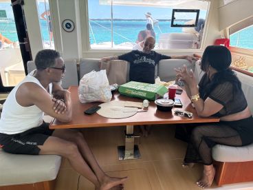 A relaxed gathering inside the cabin of a boat, featuring guests enjoying food and drinks while taking in the beautiful ocean view.