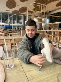 A young boy interacts with a plush toy in a modern café setting, showcasing a casual moment indoors.