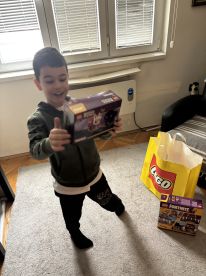 A young boy excitedly holds a LEGO box in a living room setting, showcasing his joy with new toys.