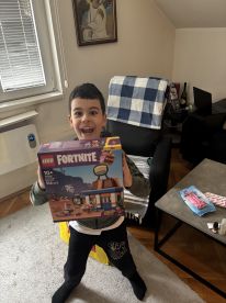 A young boy excitedly holds a LEGO Fortnite set, showcasing a joyful moment in a cozy indoor setting.