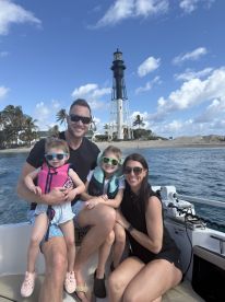 A joyful family poses on a boat with a lighthouse in the background, capturing a memorable day on the water filled with fun and adventure.