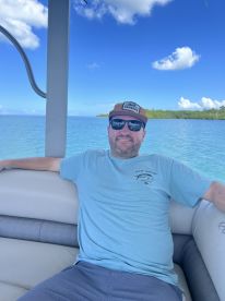 A man relaxes on the deck of a boat, enjoying the serene waters and clear skies — a perfect moment for leisure on the water.