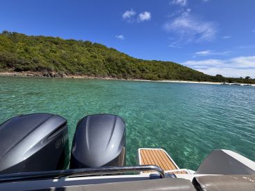 A scenic view of a boat's outboard engines with a lush green shoreline in the background, showcasing the beauty of clear turquoise waters.