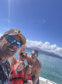 A joyful family poses for a selfie on a boat, showcasing their fun day out on the water with life jackets and smiles all around.
