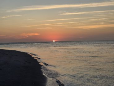 A stunning sunset over the tranquil waters, casting vibrant colors across the sky and reflecting on the beach — a perfect moment for relaxation and reflection.